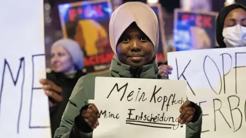 Getty Images Hadiya, an 11-year old student, attends a protest, organized by coalition of 20 civil society organizations in Austria, against the headscarf ban in schools, in Vienna, Austria on February 13, 2026. She is holding a banner which says "my headscarf, my decision"