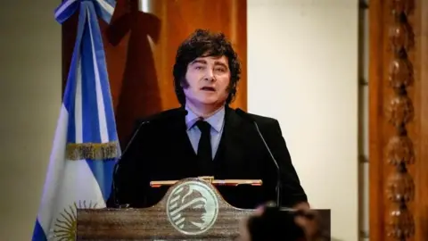 REUTERS/Mariana Nedelcu Argentine President speaks during a ceremony commemorating the 172nd anniversary of the Buenos Aires Stock Exchange in Buenos Aires, Argentina, July 16, 2026. He is wearing a dark suit with a black tie and a light blue shirt. He stands at a lectern and to his left there is an Argentine flag.