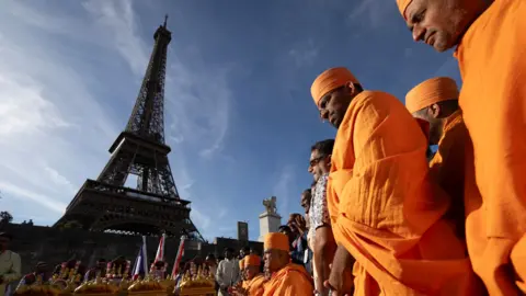 Kenzo TRIBOUILLARD/ Getty Images Hindu monks stand in front of the Eiffel Tower wearing traditional orange robes.